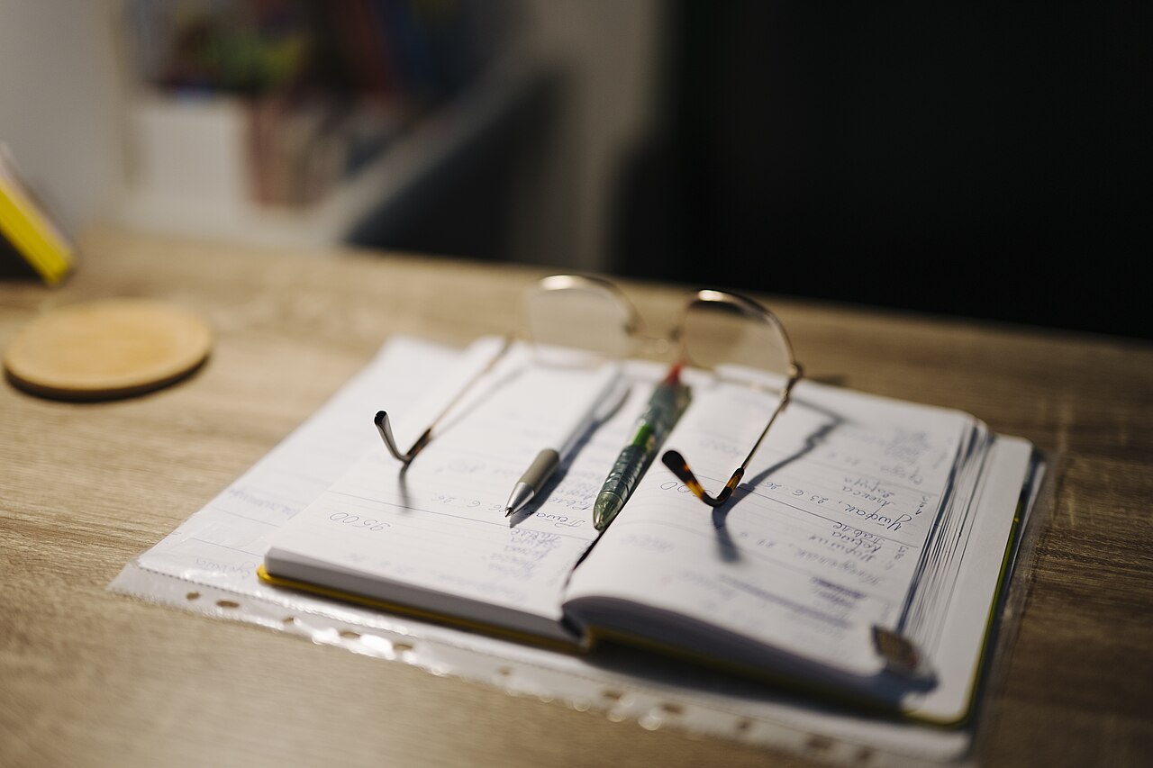 Open notebook with pens and glasses on a desk
